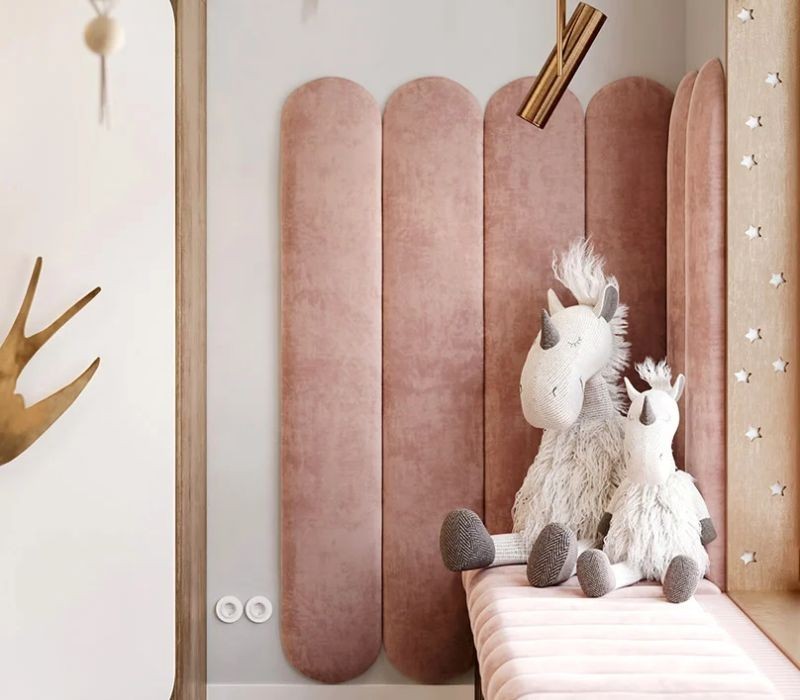 Panneaux muraux en velours rose dans une chambre d'enfant avec des peluches de zèbre et petit plug décoratif au mur.